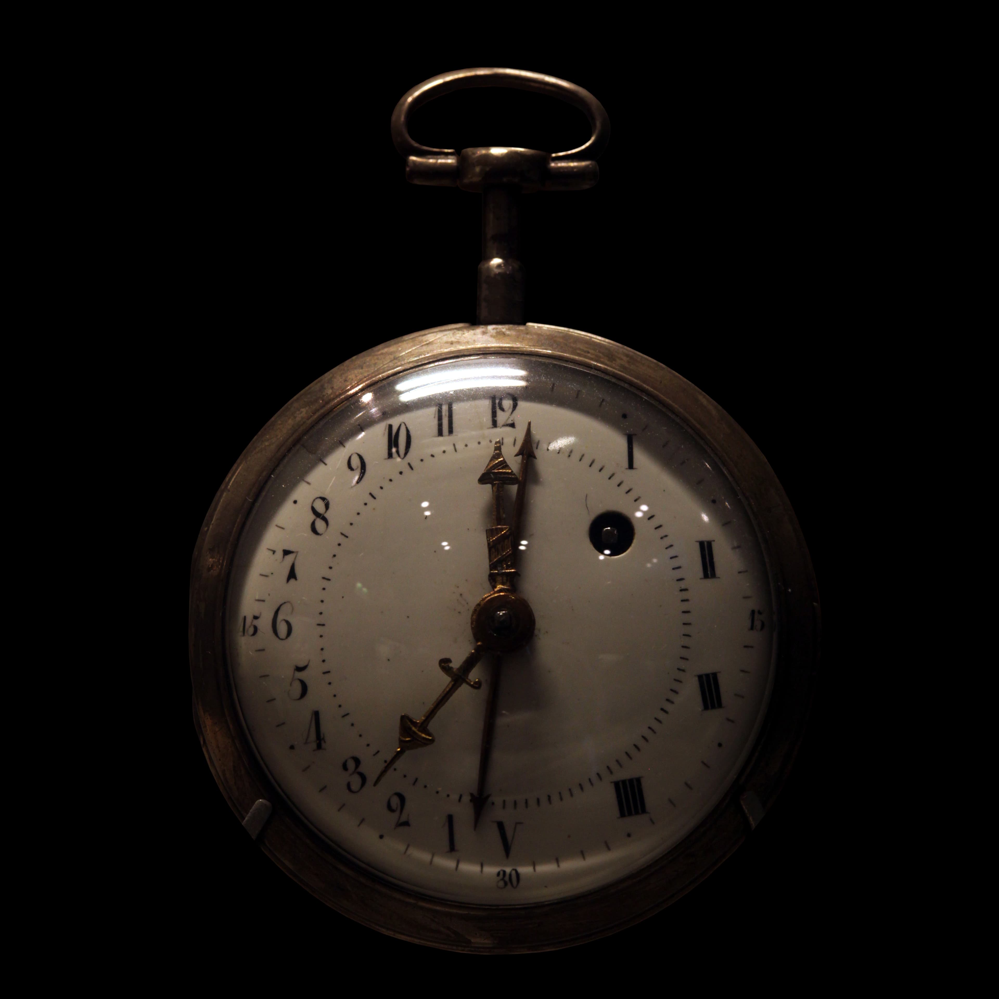 An antique pocket watch with an enamel dial marked with two competing sets of hour numerals.