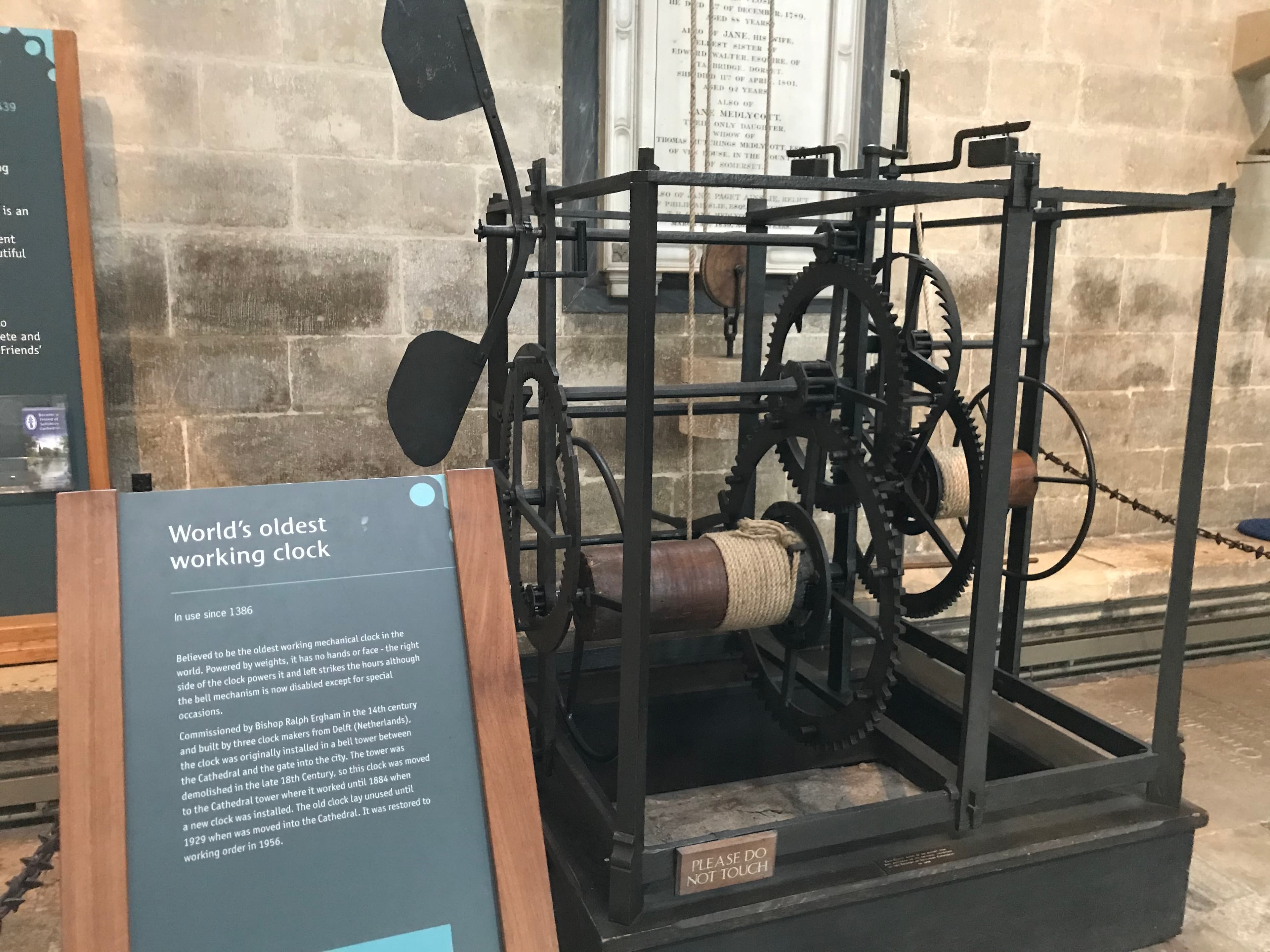 A large open iron clock mechanism of gears, weights and ropes standing on a stone cathedral floor.